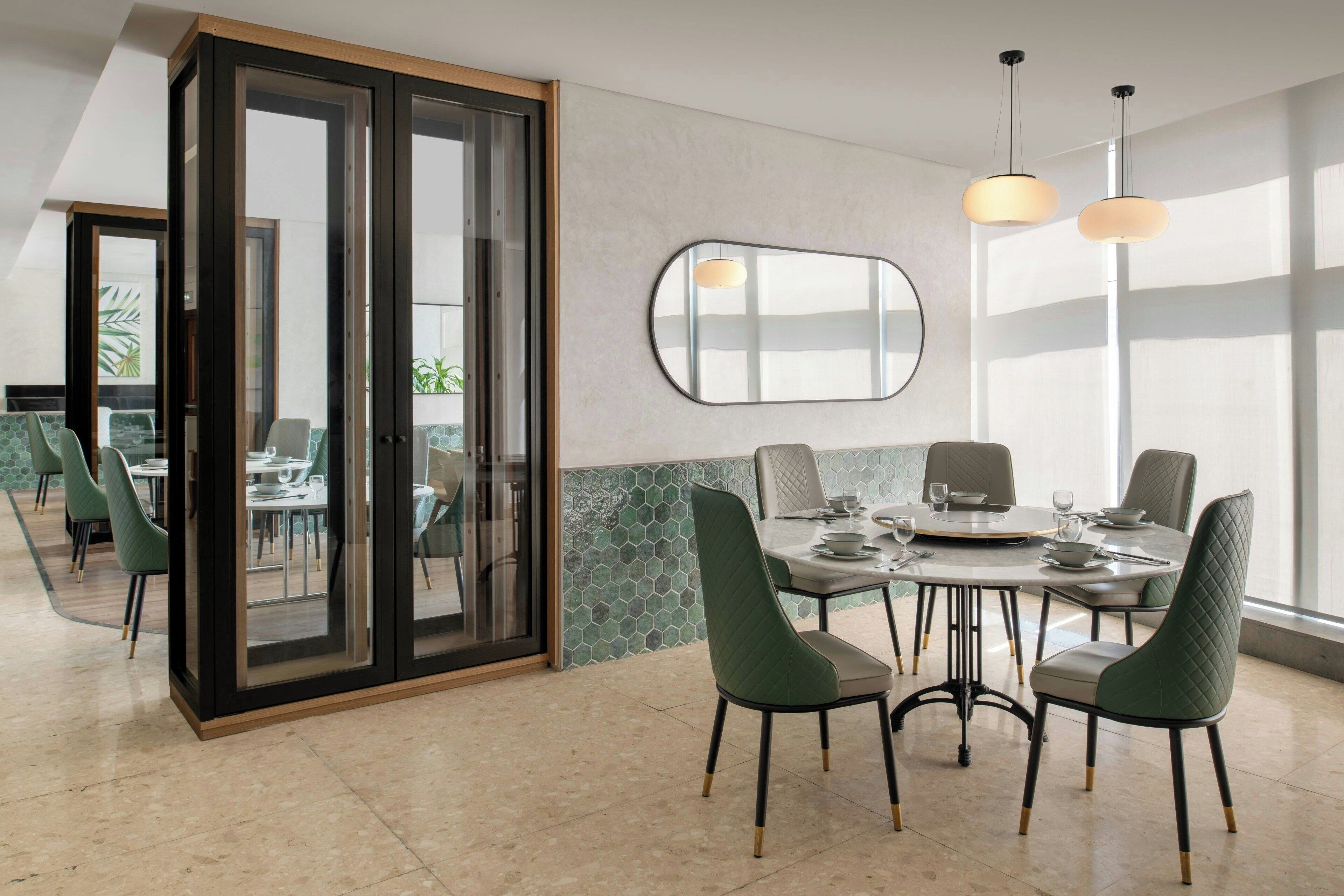 Een eetgedeelte met een ronde tafel, groene fauteuils en een glazen scheidingswand.