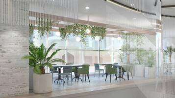 A modern indoor space with a long table and chairs, large windows, and hanging plants.