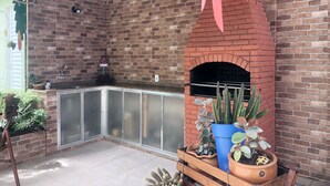 Una cocina al aire libre con horno de ladrillo, un lavamanos y diversas plantas en macetas.