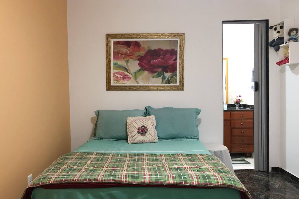 Quarto com cama, quadro floral emoldurado e penteadeira com espelho.