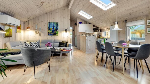Een modern interieur met een houten plafond, een eethoek met een tafel en stoelen, een bank met kussens, en een keuken met kastjes en een koelkast.