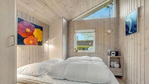 Een slaapkamer met een bed, houten wanden, een raam en kunstwerken.