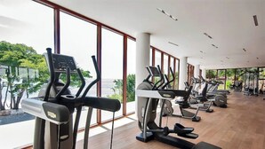 Une salle de sport équipée de plusieurs tapis de course et d’appareils d’exercice, dotée de grandes fenêtres et offrant une vue sur la verdure environnante.