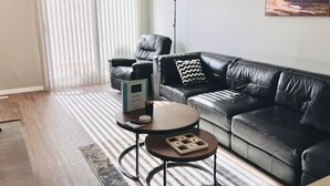A modern living room with a black leather sofa, a round coffee table, and a black leather armchair. There is a floor lamp and a painting on the wall. - Spacious 2-bedroom apartment (Camrose)