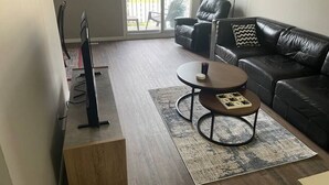 A modern living room with a flat-screen TV, a leather sofa, a coffee table, and a patterned rug. - Spacious 2-bedroom apartment (Camrose)