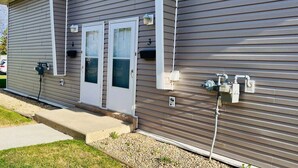 A building with two white doors, a small porch, and exterior electrical boxes. - Spacious 2-bedroom apartment (Camrose)