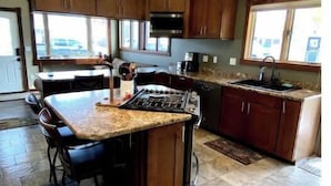 Cucina con isola centrale, pensili in legno scuro, piano cottura in acciaio inossidabile e un'ampia finestra che permette l'illuminazione naturale.