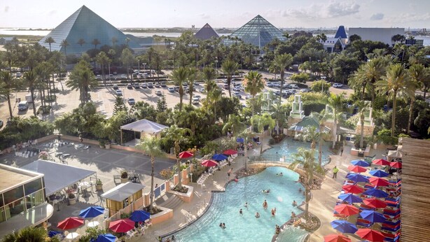 Um resort com uma piscina grande, palmeiras e estruturas piramidais ao fundo.