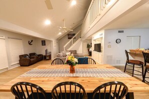 A spacious living area with a wooden dining table, chairs, a sofa, and a staircase leading to an upper level. - Just steps to the Beach, Two Min Walking Distance (Galveston)