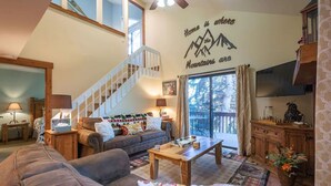 Ein gemütliches Wohnzimmer mit Treppe, großem Fenster und einer Wanddekoration mit der Aufschrift "Home is where the mountains are".