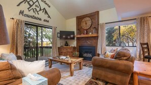 Ein gemütliches Wohnzimmer mit Kamin, Fernseher und einem großen Fenster mit Vorhängen.