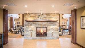 A spacious lobby with a stone fireplace, wooden flooring, and a dining area with chairs and tables. - Accessible 1-Bedroom Suite, Roll-In Shower (Folsom)