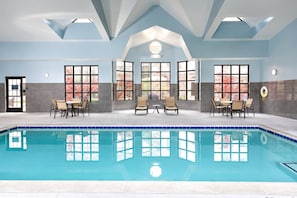 Ein überdachter Pool mit Fliesenboden, umgeben von Sitzbereichen und großen Fenstern.