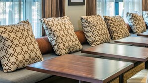 A seating area with patterned cushions and wooden tables, likely in a hotel or restaurant. - Accessible 1-Bedroom Suite, Roll-In Shower (Folsom)