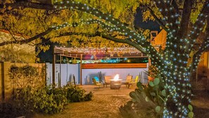 Relax by the fire pit in a serene outdoor space surrounded by comfortable seating and a tree with twinkling lights.