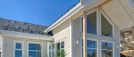 A two-story house with large windows, a balcony, and a covered outdoor seating area.