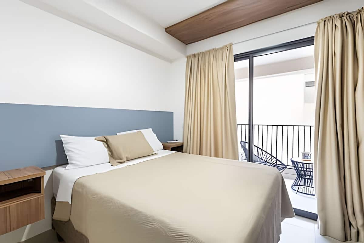 Ein Hotelzimmer mit Bett, Nachttisch, Holz-Kopfteil, Balkon mit Geländer und Vorhängen.