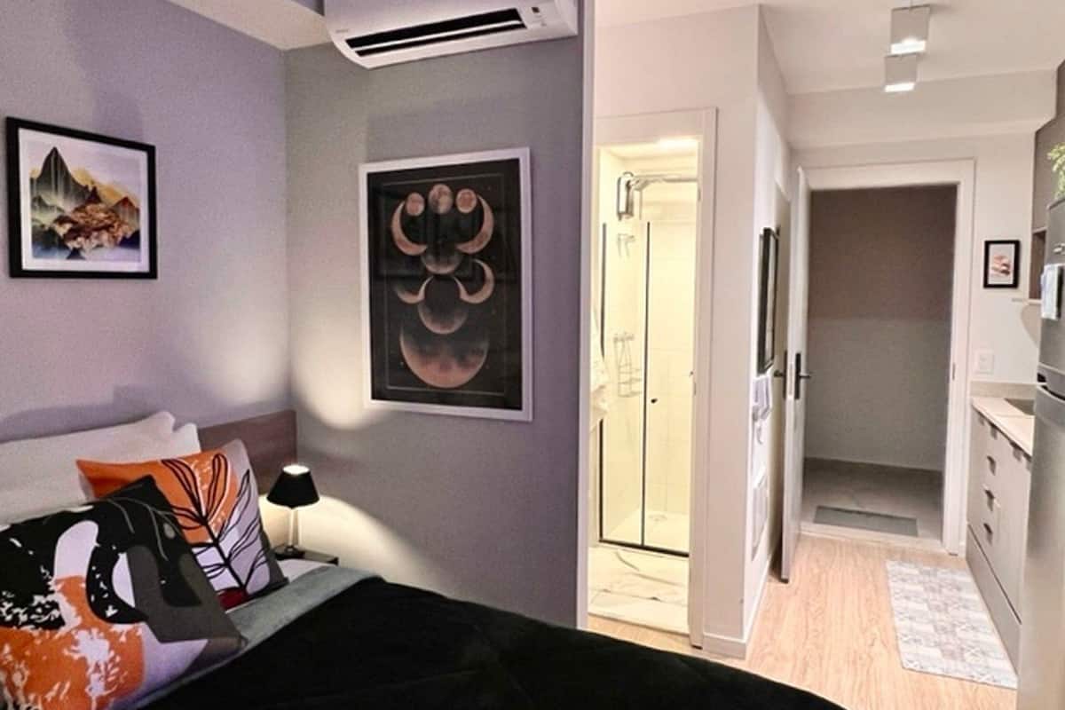 Ein modernes Schlafzimmer mit Bett, Nachttisch, Wand-Klimaanlage und einer Tür zu einem Badezimmer.