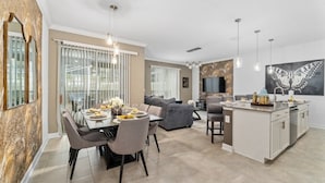 A modern kitchen with a central island, dining area with a table and chairs, and a living area with a sofa and a TV.
