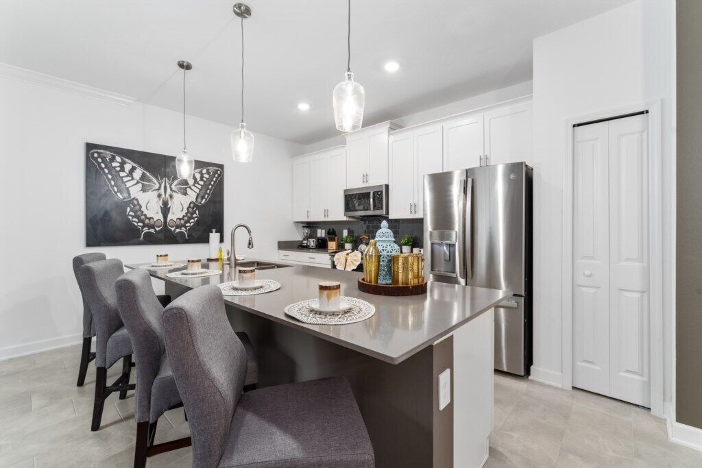 A modern kitchen with white cabinets, a central island with bar stools, stainless steel appliances, and pendant lighting.