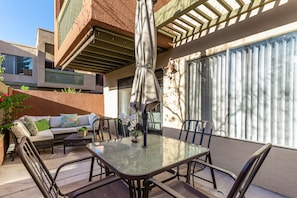 Un patio exterior con una mesa de vidrio, sillas, un sofá y una sombrilla.