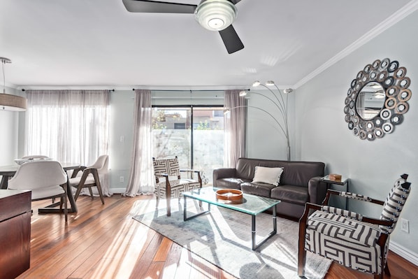 Una sala de estar moderna con una mesa de centro de vidrio, un sofá de cuero y un comedor con una mesa y sillas blancas.