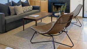 A modern living room with a sofa, coffee table, and two wicker chairs. There is a fireplace, a ceiling fan, and a TV mounted on the wall. - Flawless One Bedroom Old Town Scottsdale Condo (Scottsdale)