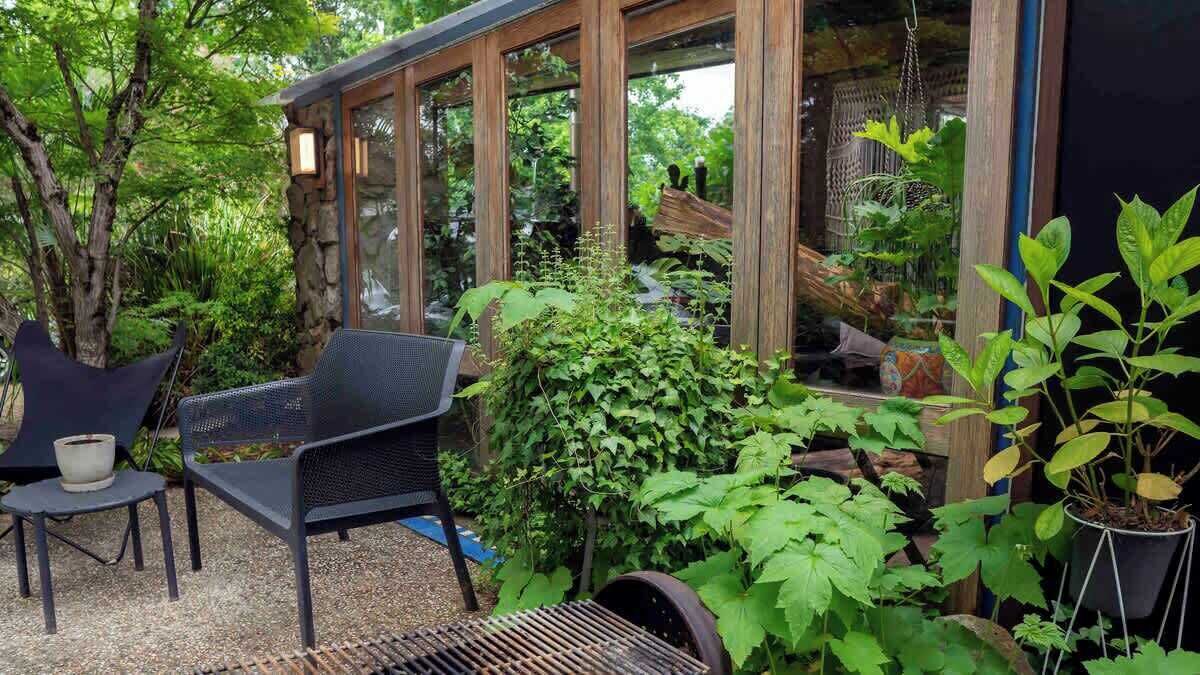 Un patio con una parrilla, mobiliario exterior y vista a un jardín a través de una estructura de madera.