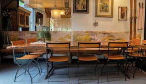 Zona pranzo con tavoli e sedie in legno, una pianta in vaso e opere d'arte appese al muro.