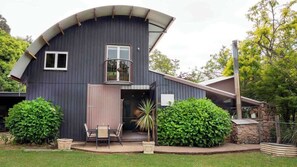 A modern house with a curved roof, a balcony, and a small porch area with chairs.