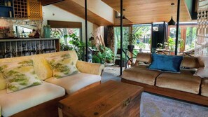 A cozy living area with two sofas, a wooden coffee table, and a bar area with shelves and plants.
