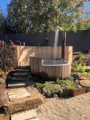 Una vasca idromassaggio in legno circolare con elemento decorativo, immersa in un giardino ricco di piante e rocce.