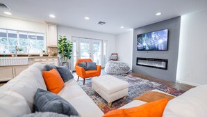 A modern living room with a white sofa, orange armchair, and a flat-screen TV mounted on the wall. - Spacious Scottsdale home with resort yard, heated pool included in price! (Scottsdale)