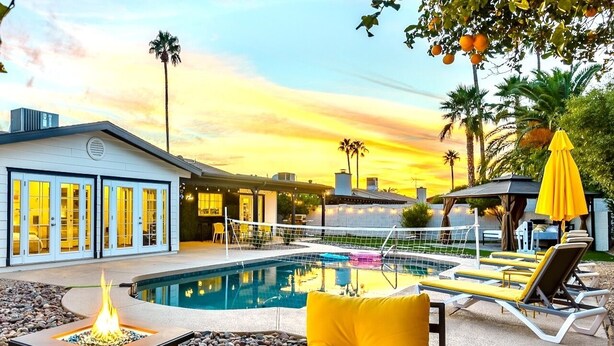 A pool area with a fire feature, lounge chairs, and a building with large windows. - Spacious Scottsdale home with resort yard, heated pool included in price! (Scottsdale)