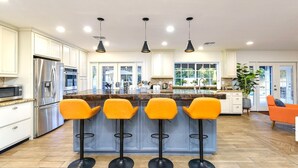 A modern kitchen with four bar stools, a large island, and a refrigerator. - Spacious Scottsdale home with resort yard, heated pool included in price! (Scottsdale)