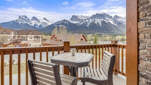 A balcony with a table and chairs, overlooking a mountain range. - 3 Sisters Mountain Views | Hot Tub & Heated Pool (Canmore)