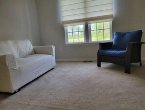 Una habitación con un sofá blanco y una silla de mimbre oscura.