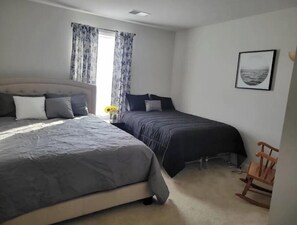 Un dormitorio con dos camas, una ventana con cortinas, un cuadro enmarcado en la pared y una mecedora de madera.
