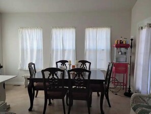 Ein Essbereich mit Tisch und vier Stühlen, eine rote Kommode mit Flaschen und ein Fenster mit Vorhängen.