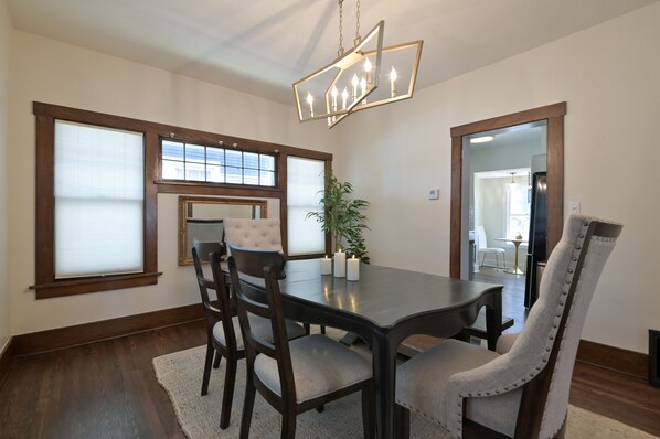 A dining room with a dark wooden table, four upholstered chairs, a chandelier, and a potted plant. - Midtown Manor: Full Kitchen + A/C + Backyard + Washer & Dryer (Omaha)