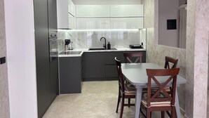 Une cuisine moderne avec des meubles gris, un plan de travail blanc et un coin repas comprenant deux chaises en bois et une table.