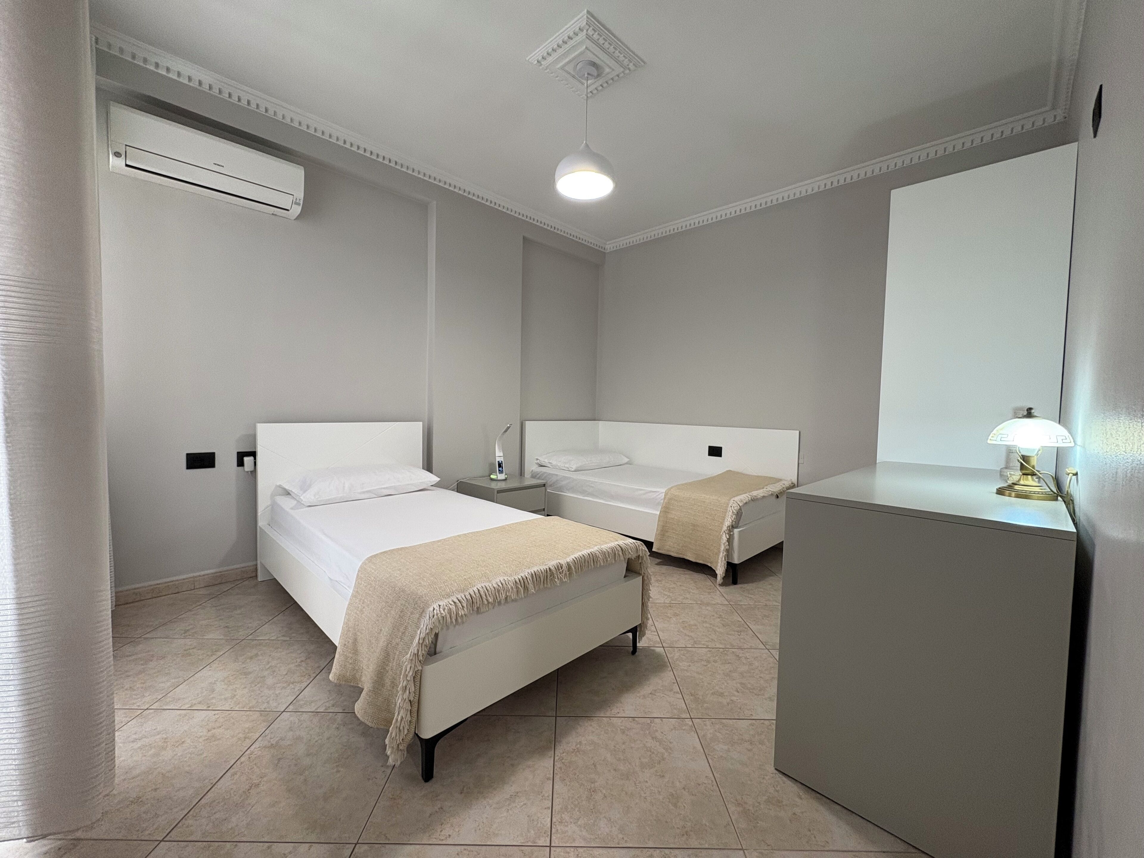 Habitación de hotel con dos camas, un escritorio, un espejo y aire acondicionado.