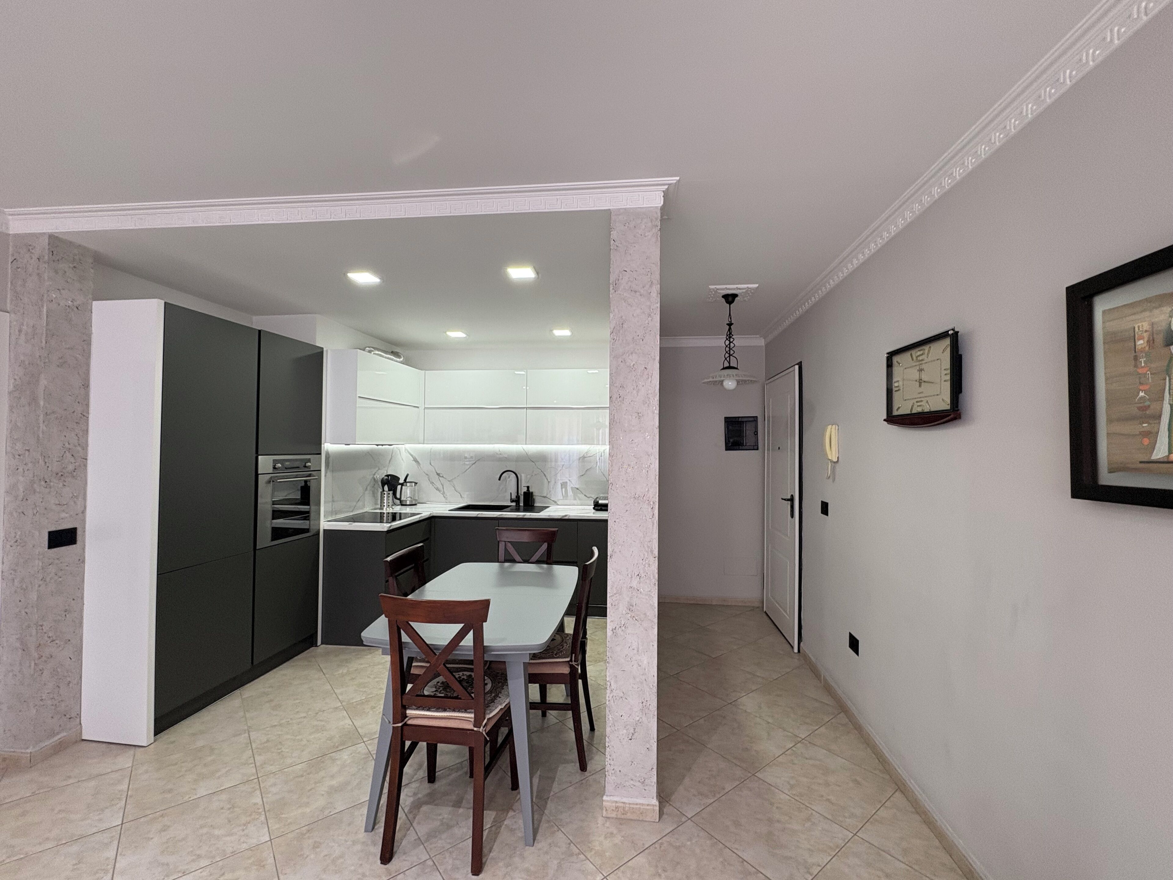 Une cuisine moderne avec des meubles de couleur sombre, un plan de travail blanc et un coin repas comprenant une table et des chaises.
