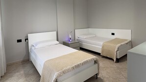 Une chambre d’hôtel avec deux lits simples, une table de chevet avec une lampe, un appareil de climatisation et un petit bureau avec une chaise.
