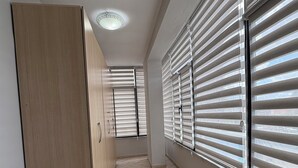 Un couloir avec une armoire en bois, un sol carrelé et des fenêtres équipées de stores.