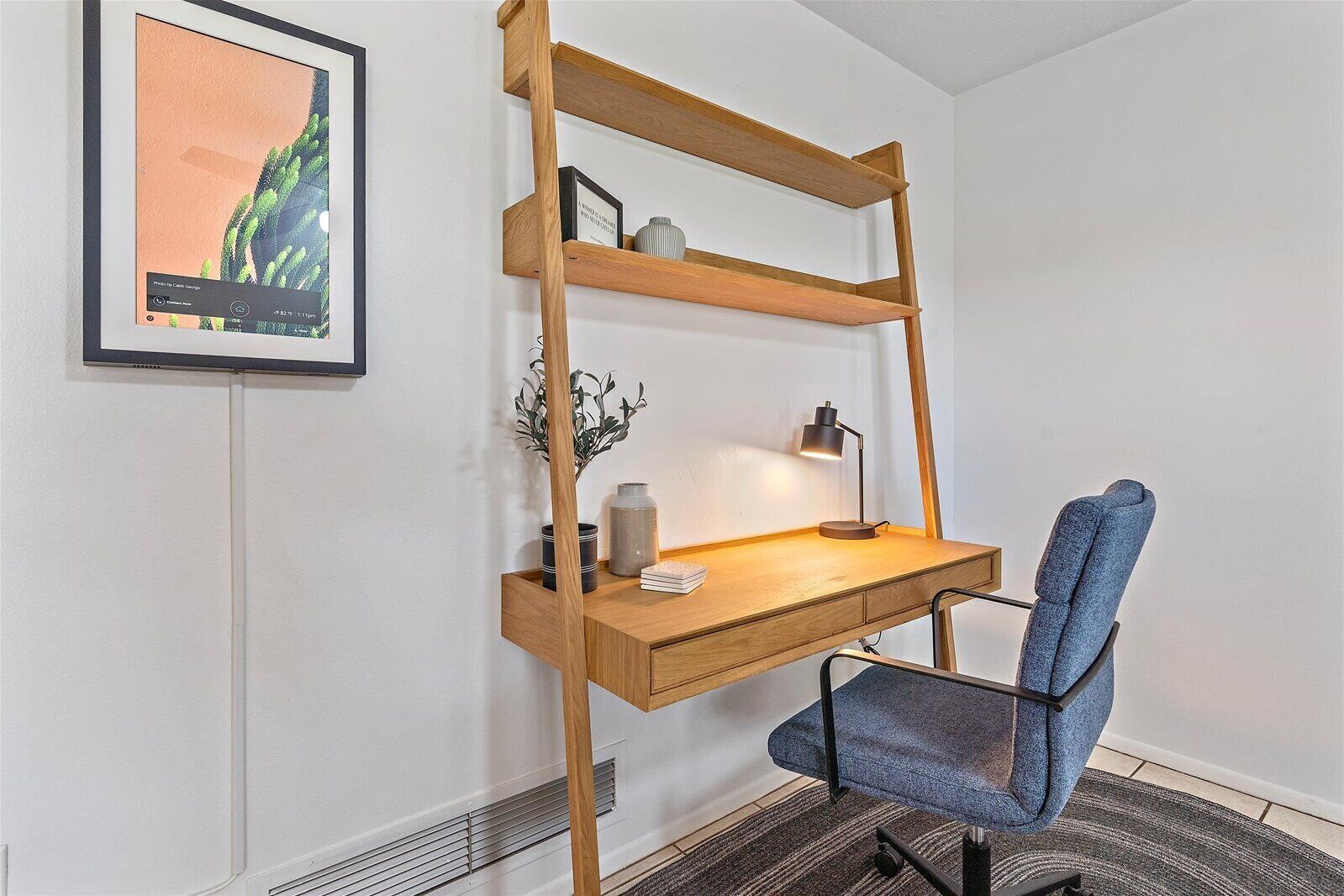 A compact workspace with a wooden desk, a blue chair, and a wall-mounted shelf.