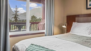 Una habitación de hotel con una cama grande, una mesita de noche, una lámpara y una ventana con vistas a montañas y árboles.