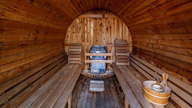 Una sauna con paredes y bancos de madera, una unidad de calefacción central y un cubo de madera.