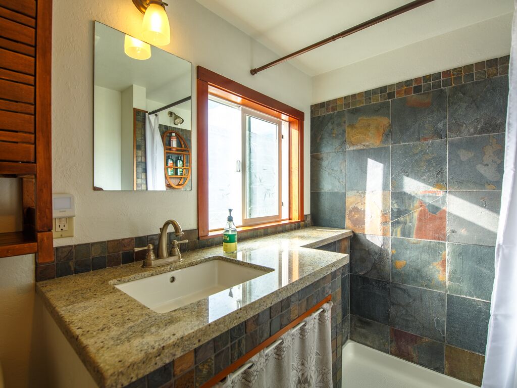 A bathroom with a granite countertop sink, a mirror, a shower with a glass door, and a tiled wall.
