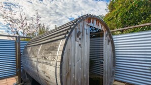 Una estructura cilíndrica de madera con una puerta, posiblemente una sauna u otra instalación similar, rodeada de cercas metálicas.